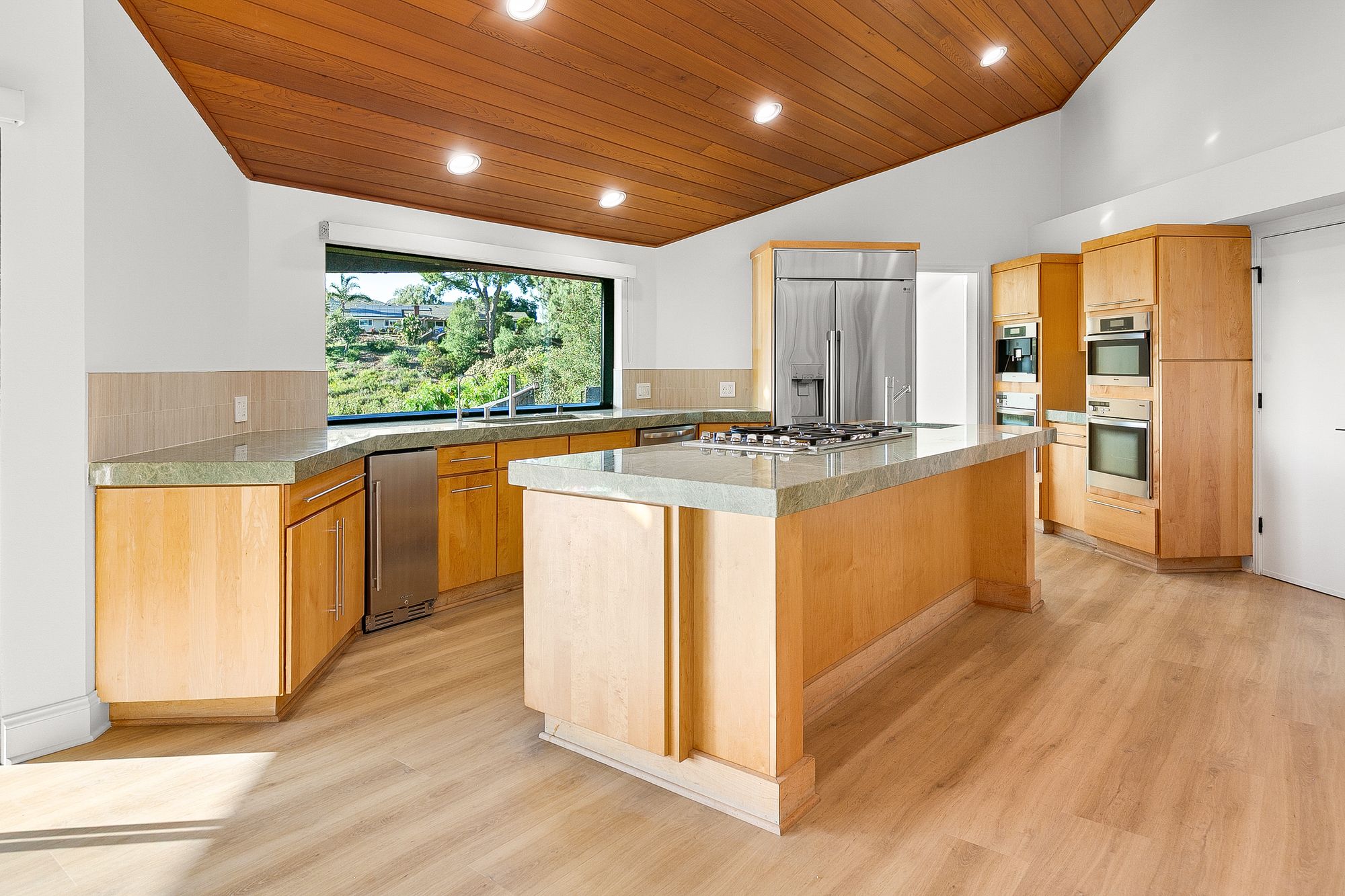 Kitchen with maple cabinets, a vaulted wood ceiling, and a wide window to the yard