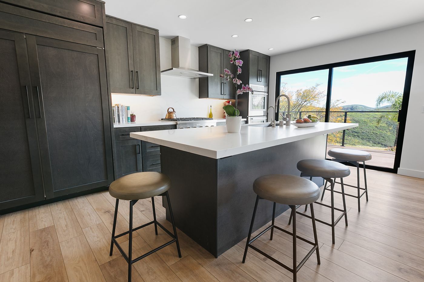 Kitchen with dark cabinetry, white countertops, and a wall of glass opening to the yard